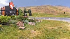 A sign for 'Elkhorn in Sun Valley' with a deer logo, surrounded by greenery and a road. - Lovely condo w/ beautiful views & shared pool/hot tub/tennis/golf (Sun Valley)