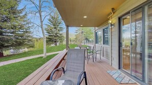 A covered outdoor deck with a table and chairs, a sliding door, and a view of trees and a grassy area. - Lovely condo w/ beautiful views & shared pool/hot tub/tennis/golf (Sun Valley)