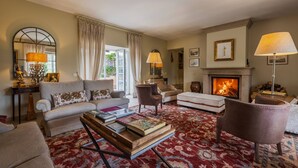Un salon avec une cheminée, des canapés, des fauteuils et une table basse sur laquelle sont posés des livres.