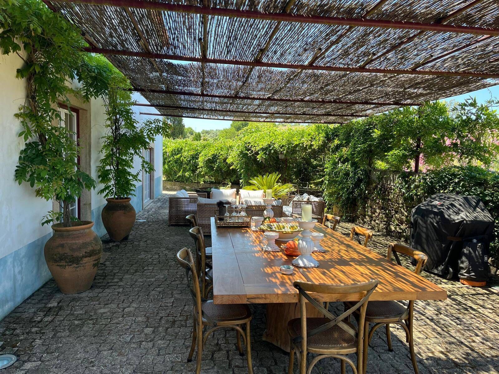 An outdoor dining area with a table set for four, surrounded by wicker chairs, under a woven shade structure.