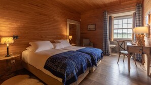 Une chambre dans un chalet en bois, comprenant un lit, deux tables de chevet, un bureau, une chaise et une fenêtre avec des rideaux.