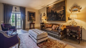 Un salon avec un canapé, un pouf et un grand tableau accroché au mur.
