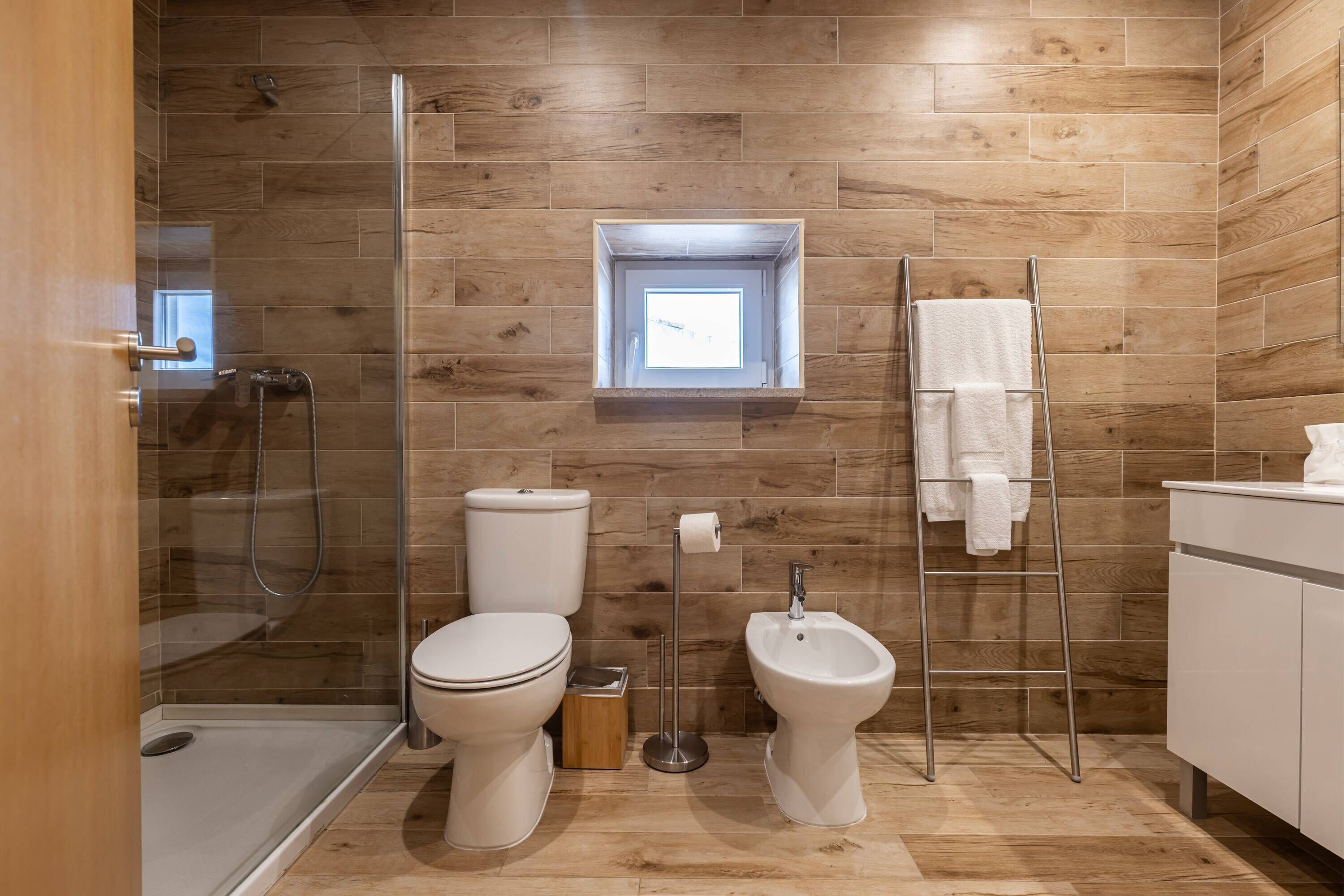 Un baño moderno con ducha, inodoro, bidé y una ventana pequeña.