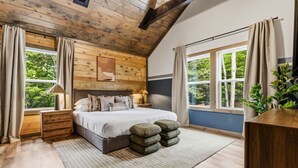 Un dormitorio con techo de madera, una cama con almohadas, una mesita de noche, una ventana con cortinas y una planta.
