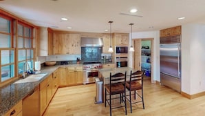 A modern kitchen with wooden cabinets, granite countertops, stainless steel appliances, and pendant lighting. - Modern mountain penthouse close to hikes & skiing (Sun Valley)