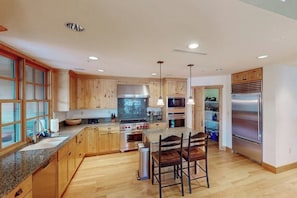 Una cocina moderna con armarios de madera, encimeras de granito, electrodomésticos de acero inoxidable e iluminación colgante.