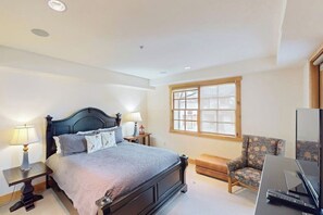 Un dormitorio con cama, lámparas de noche, una silla, un televisor y una ventana.