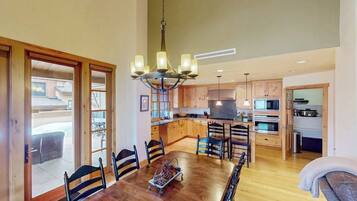 A spacious dining area with a wooden table and chairs, a chandelier, and a view of the outside.