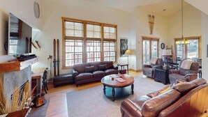 A spacious living room with a fireplace, leather sofas, a coffee table, and large windows. - Modern mountain penthouse close to hikes & skiing (Sun Valley)