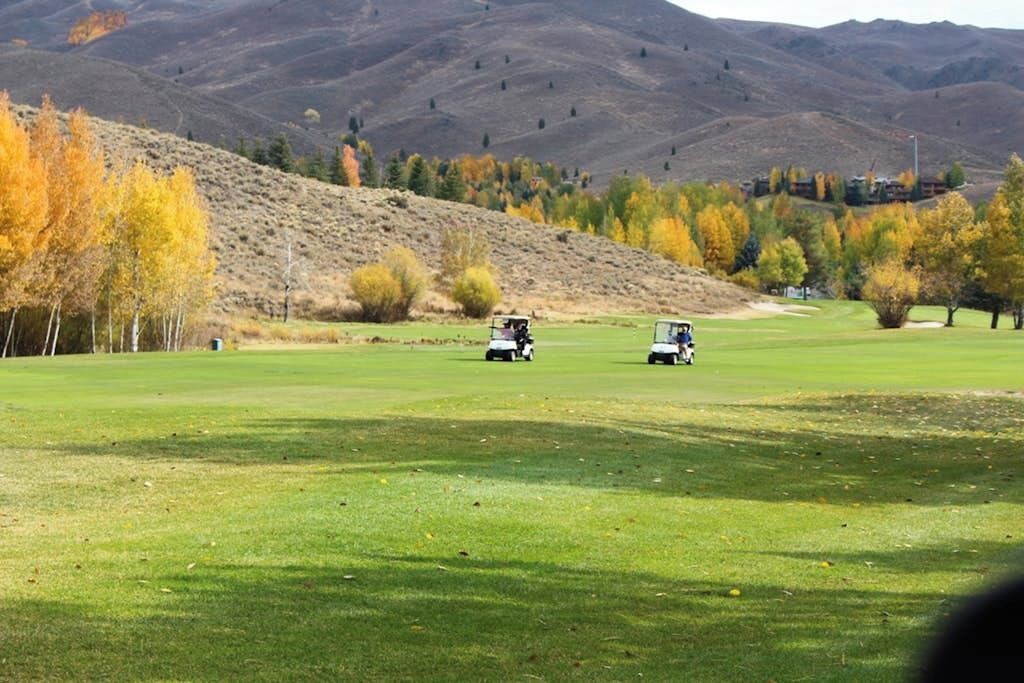 Un campo de golf con dos carritos de golf, un paisaje montañoso y árboles de colores otoñales.