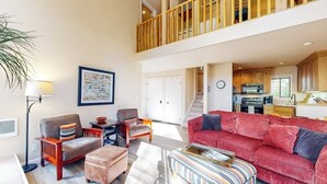 A spacious living area with a red sofa, a striped ottoman, a wooden coffee table, and a floor lamp. There is a staircase leading to an upper level with wooden railings. - Pleasant condo with private washer/dryer (Sun Valley)