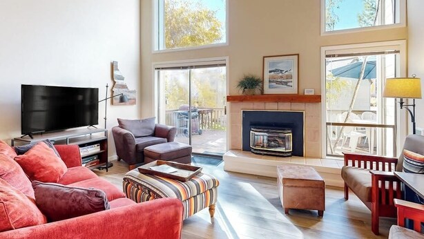 A spacious living room with a fireplace, large windows, a flat-screen TV, and a cozy seating area. - Pleasant condo with private washer/dryer (Sun Valley)