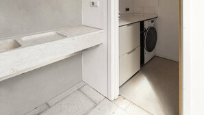 Een wasruimte met een wasmachine, een wasbak en een wandcontactdoos.