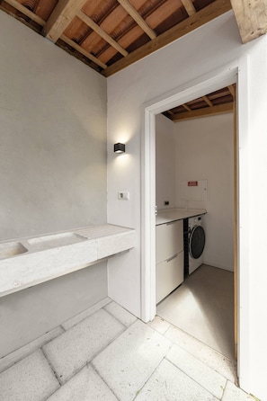 Un espace buanderie comprenant un lave-linge, un évier et une boîte électrique fixée au mur.