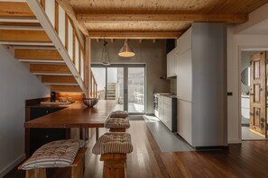 Une cuisine moderne avec des poutres en bois, un coin repas avec des bancs et une vue sur l’extérieur.
