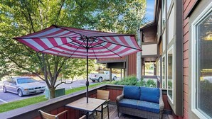 Eine überdachte Terrasse mit Tisch, Stühlen, einer Couch und einem gestreiften Sonnenschirm.
