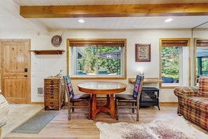 Une table à manger en bois avec des chaises, un canapé, une commode et un tapis en peau de vache dans une pièce dotée de poutres en bois et de grandes fenêtres.