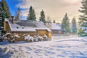 Eine Hütte mit geneigtem Dach, umgeben von schneebedeckten Bäumen und einem Zaun.