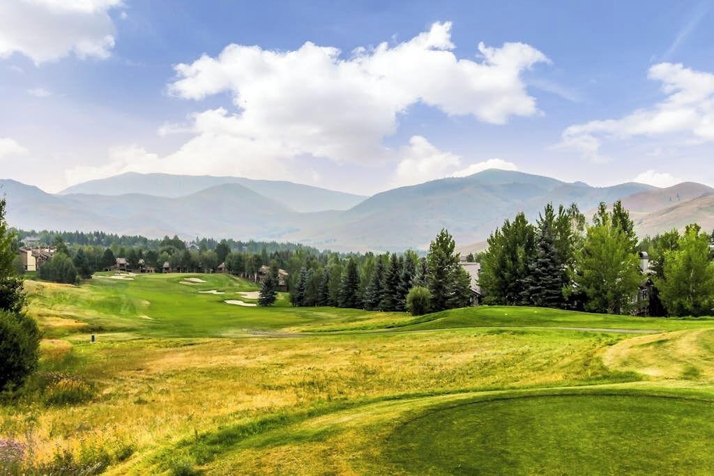 Un parcours de golf avec des collines douces, des arbres et des montagnes lointaines, le tout sous un ciel dégagé.