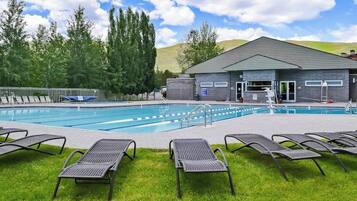 A swimming pool with lounge chairs, a building with a grey roof, and trees in the background.