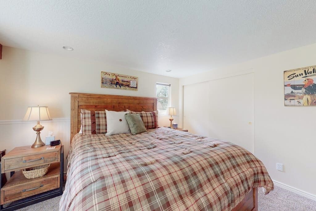 A bedroom with a wooden headboard, a plaid bedspread, a nightstand with a lamp, and a wall poster.
