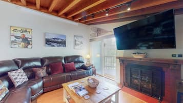 A living room with a leather sofa, a wooden coffee table, a fireplace, and a large TV mounted on the wall.