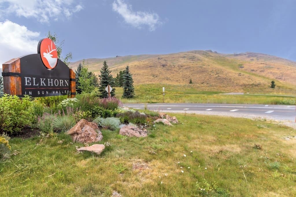 Letrero que dice 'Elkhorn in Sun Valley' con un logotipo de ciervo, rodeado de follaje y una carretera.