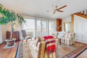 Un salon spacieux avec une grande fenêtre, un ventilateur de plafond et une plante en pot.