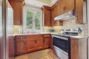 Une cuisine avec des meubles en bois, une cuisinière, un four à micro-ondes et une fenêtre donnant sur les arbres.