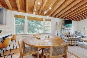 Ein Essbereich mit einem runden Holztisch, Korbstühlen und einer Decke mit freiliegenden Balken.