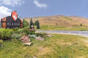 Schild für 'Elkhorn in Sun Valley' mit einem Hirsch-Logo, umgeben von Grünpflanzen und einer Straße.