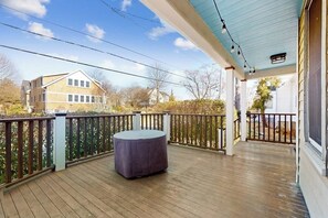 Eine Holzterrasse mit einem runden Tisch, eine überdachte Veranda mit Lichterketten und ein Blick auf ein Haus im Hintergrund.