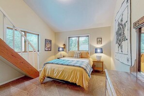 Une chambre à coucher comprenant un lit, deux tables de chevet, une commode, un escalier et une grande fenêtre.