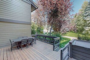 Eine Terrasse mit Tisch und Stühlen, umgeben von einem Holzzaun, mit einem Baum und Grünpflanzen im Hintergrund.