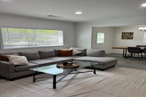 A modern living room with a sectional sofa, a glass coffee table, and a dining area with a table and chairs. - Cozy ATL Stay Fast Wi-Fi + Close to Everything (Atlanta)