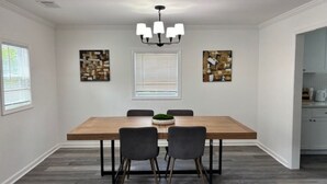 Un comedor con mesa de madera, cuatro sillas, una araña y dos cuadros abstractos en las paredes.