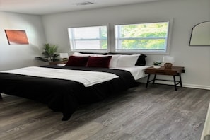 A bedroom with a bed, two windows, a nightstand, a plant, and a wall-mounted mirror. - Cozy ATL Stay Fast Wi-Fi + Close to Everything (Atlanta)