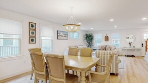 Ein Essbereich mit Holztisch und Stühlen, einer Chandelierleuchtre und einer Couch im Hintergrund.