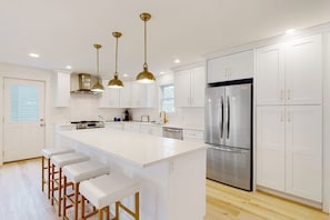 A modern kitchen with white cabinets, stainless steel appliances, and a central island with bar stools.