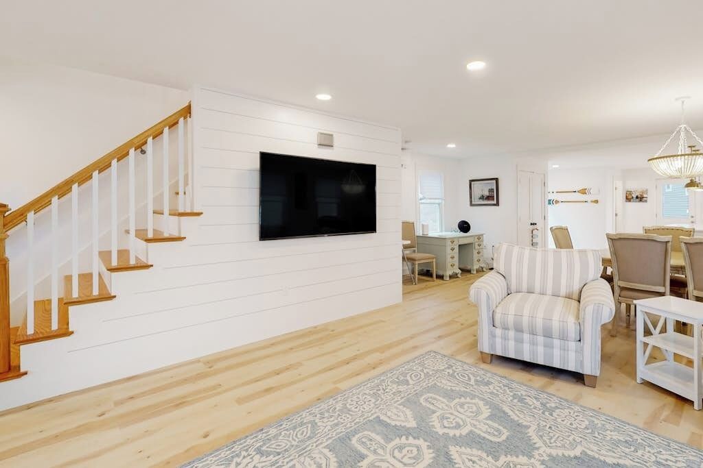 Un salon avec un escalier en bois, un téléviseur à écran plat, un fauteuil à rayures et un tapis à motifs.