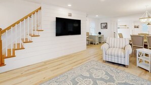 Ein Wohnzimmer mit einer Holztreppe, einem Flachbildfernseher, einem gestreiften Sessel und einem gemusterten Teppich.