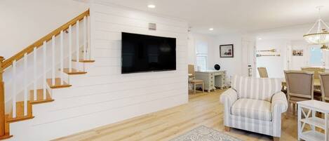 A living room with a wooden staircase, a flat-screen TV, a striped armchair, and a patterned rug.