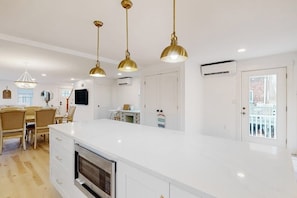 A modern kitchen with a large island, pendant lights, and a dining area with chairs. - Coastal retreat steps to the beach with smart TVs, desk, grill, children's items (Gloucester)