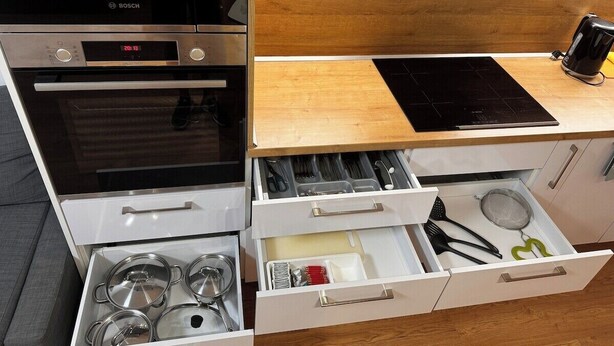 A kitchen with a Bosch oven, a built-in microwave, a wooden countertop, and a drawer with kitchen utensils.