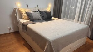 A neatly made bed with a patterned bedspread, a bedside lamp, and a power outlet on the wall.