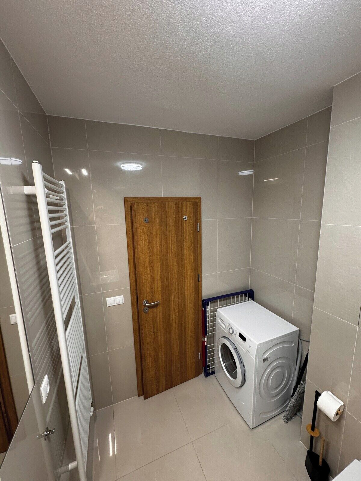 Une petite buanderie équipée d’un lave-linge, d’un étendoir et d’une porte en bois.