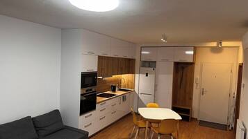 A compact living space with a kitchenette, a sofa, a dining table with chairs, and a door.