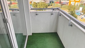 A balcony with artificial green turf, metal railings, and a view of a residential area.
