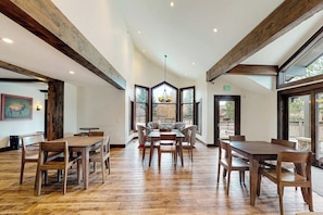 A spacious dining area with wooden tables and chairs, large windows, and a high ceiling with exposed beams. - Inviting condo with skiing, pool, fireplace, mountain view, & W/D (Sun Valley)