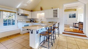 A kitchen with a central island, white cabinetry, and a dining area with chairs.